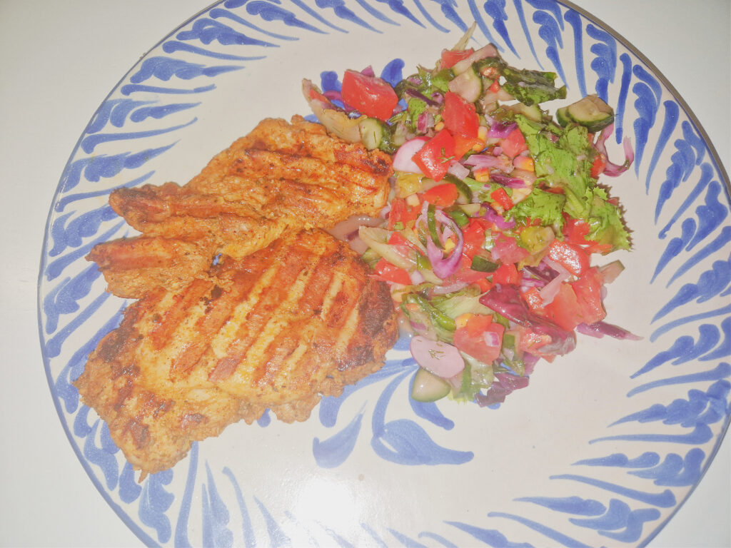 Mięso z udek kurczaka które zostało zgrillowane i nabrało pięknego złotego koloru ułożone na biało niebieskim talerzu z kolorowa sałatką