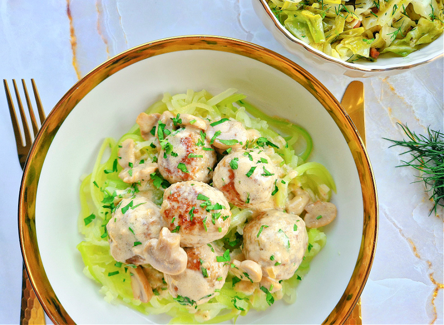 Keto pulpety w sosie pieczarkowym podane na talerzu z natką pietruszki. Zamiast makaronu, keto wersja makaronu z cukinii. Jako dodatek kapusta duszona z boczkiem