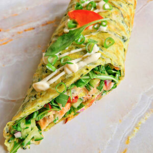 Wrap z cukinii nadziewany rukolą, łososiem, sosem czosnkowym, czerwoną cebulą i pomidorami na jasnym tle