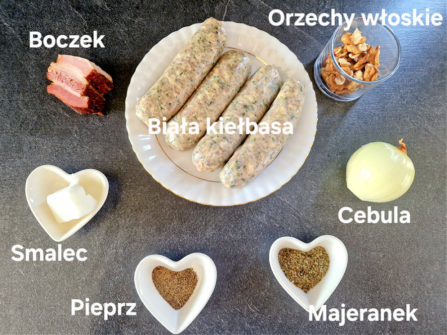 Składniki na zapiekaną białą kiełbasę – biała kiełbasa, boczek, orzechy włoskie, cebula, smalec przyprawy, ułożone w miseczkach na ciemnym blacie