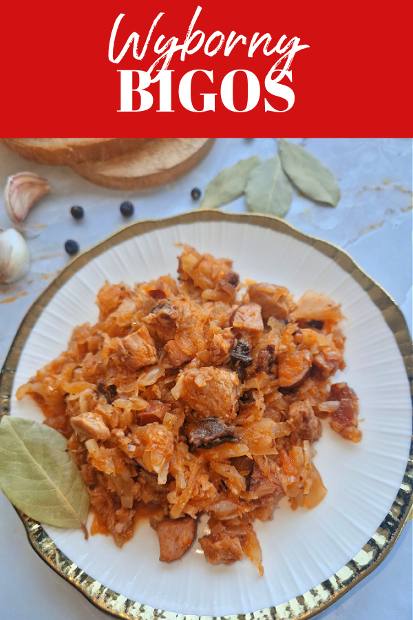 Na górze czerwone tło z białym napisem „Wyborny bigos”. Pod spodem na biało-złotym talerzyku widać bigos z mięsem, grzybami i kiełbasą. Obok talerzyka leżą przyprawy , ziele angielskie, jałowiec i ząbki czosnku