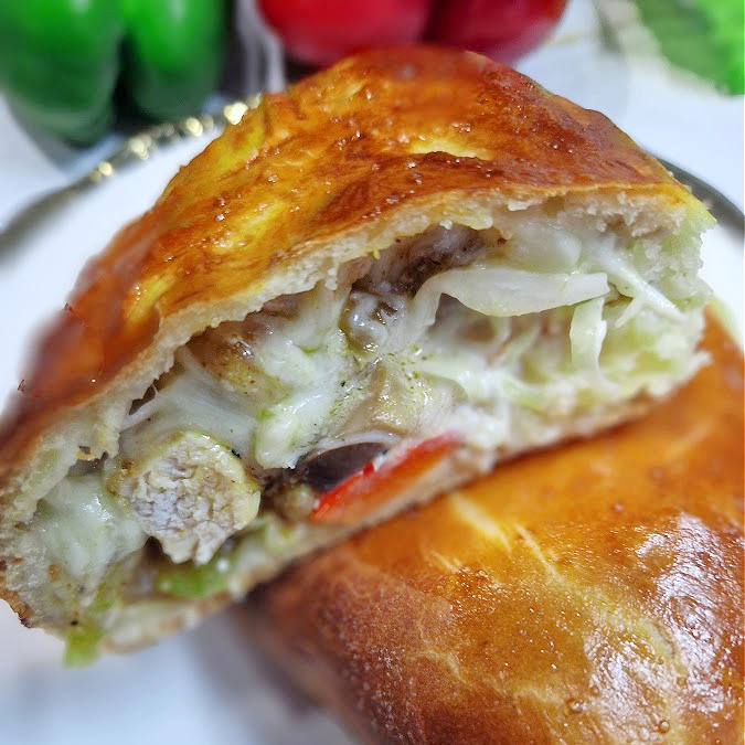 Kwadratowe zdjęcie calzone w przekroju. Widoczne mięso, kapusta, pieczarki, ser i sos. Skórka złocista. Tło jasnozłote.