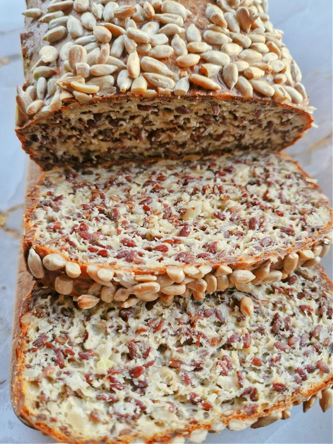 Zbliżenie na bochenek chleba twarogowego low carb z chrupiącą skórką z którego ukrojone są dwie kromki