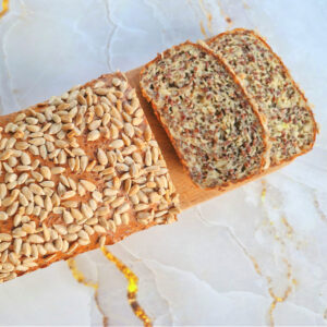 Chleb twarogowy z ziarnami ułożony na drewnianej desce do krojenia. Jasne tło z złotymi elementami.