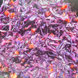 Kwadratowe zbliżenie na porcję czerwonej kapusty duszonej z boczkiem i cebulą. Danie ma intensywnie bordowy kolor i widać w nim kawałki boczku oraz podsmażonej cebuli.