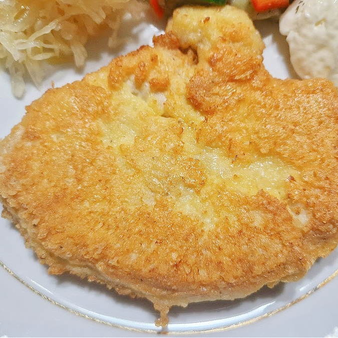 Zbliżenie na soczysty filet panierowany w serze parmezan.