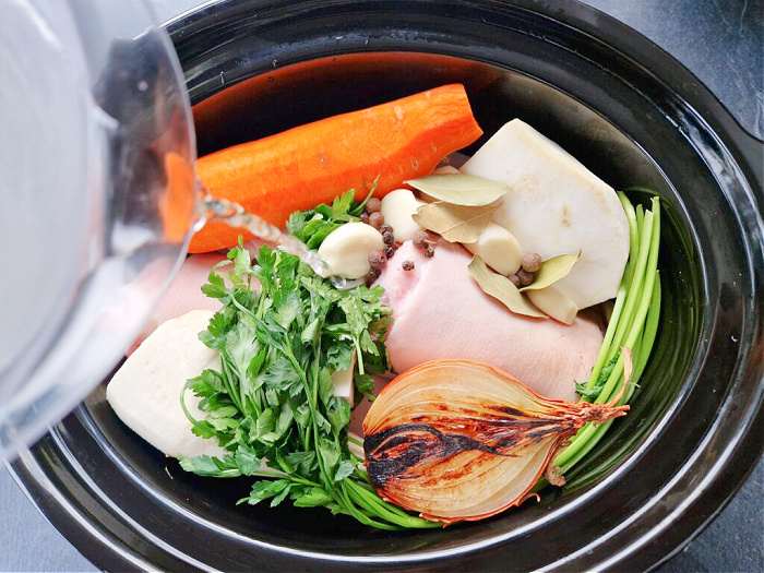 Wnętrze misy wolnowaru wypełnione składnikami na galaretkę. Widać mięso z nóżek i golonki, przypaloną cebulę, jarzyny i zieleninę. Wszystko zalewane wodą, gotowe do długiego duszenia.