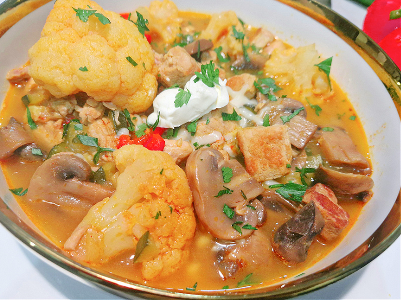 Keto gulasz z wieprzowiny z warzywami w misce z kleksem mascarpone, posypany natką pietruszki.