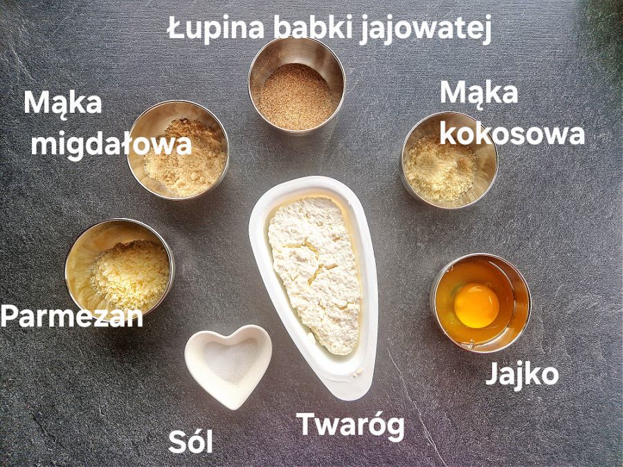Składniki do przygotowania keto klusek śląskich. Na ciemnym blacie ułożone w miseczkach: twaróg, mąka kokosowa, mąka migdałowa, parmezan, jajko i sól