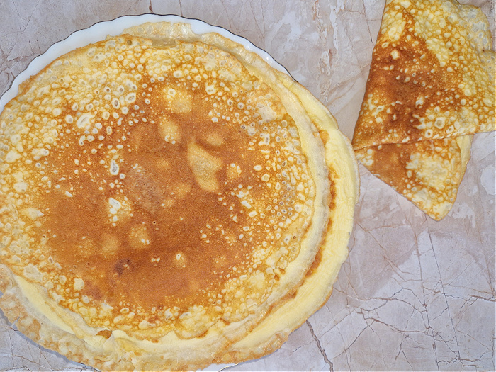Naleśniki keto ułożone warstwami na talerzu, obok zwinięty naleśnik na kremowym blacie.