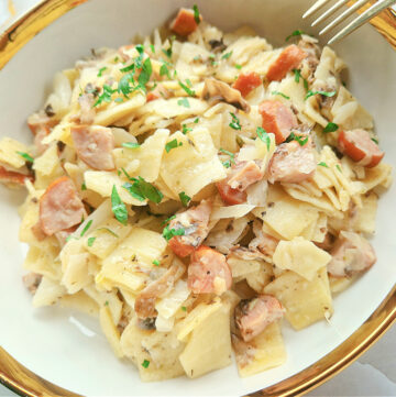 Kwadratowe główne zdjęcie: misternie podane łazanki z kapustą, pieczarkami i kiełbasą, posypane świeżą pietruszką.