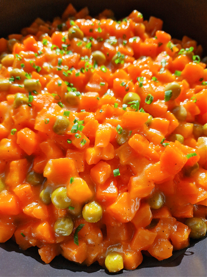 Zbliżenie na patelnię pełną marchewki oprószanej z zielonym groszkiem, danie ma apetyczny, złocisty kolor.