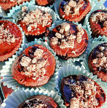 Muffinki czekoladowe ułożone na drewnianej desce. Każda w niebieskiej papilotce, posypana pokruszonym Prince Polo, w środku z ukrytą czekoladką Merci.