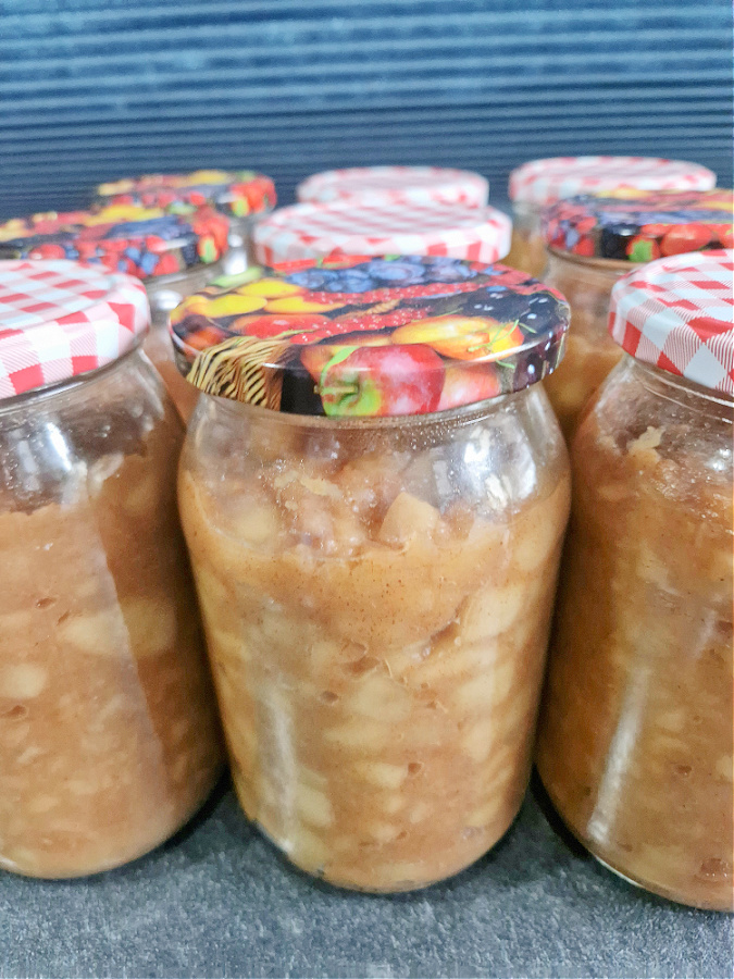 Kilka zawekowanych słoików z nadzieniem do szarlotki ustawionych na ciemnym blacie, gotowych do przechowywania na zimę.