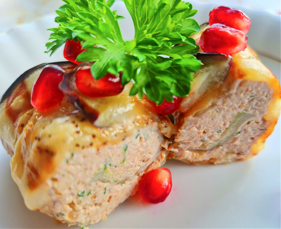 Zbliżenie na grillowane roladki bakłażanowe nadziewane masą serowo-orzechową w przekroju. Udekorowane granatem i zieloną pietruszką.