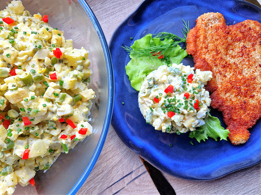 Keto sałatka jarzynowa podana na niebieskim talerzu wraz z kotletem w keto panierce. Obok miska z sałatką. Drewniany blat