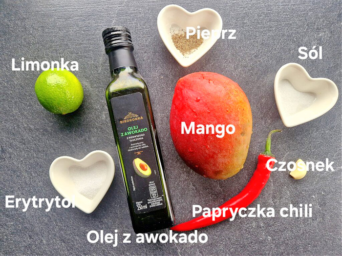 Składniki na antracytowym blacie: w pojemniczkach przyprawy, a obok limonka, erytrytol, olej z awokado, czerwona papryczka chili, czosnek, mango, sól i pieprz.