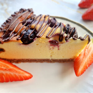 Zbliżenie na niskoweglowodanowy keto sernik z borówkami. Podany na białym talerzyku z kawałkami truskawek. Jasne tło