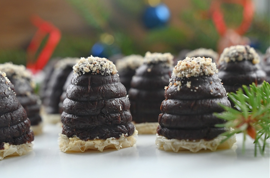 Ujęcie z boku ukazujące ciasteczka „ule” ułożone na białym blacie. W tle widoczne są ozdoby świąteczne i gałązki choinki.