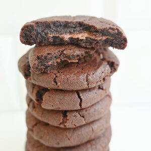 Zdjęcie główne kwadratowe. Ciastka czekoladowe nadziewane nutellą ułożone jedno na drugim na jasnym tle