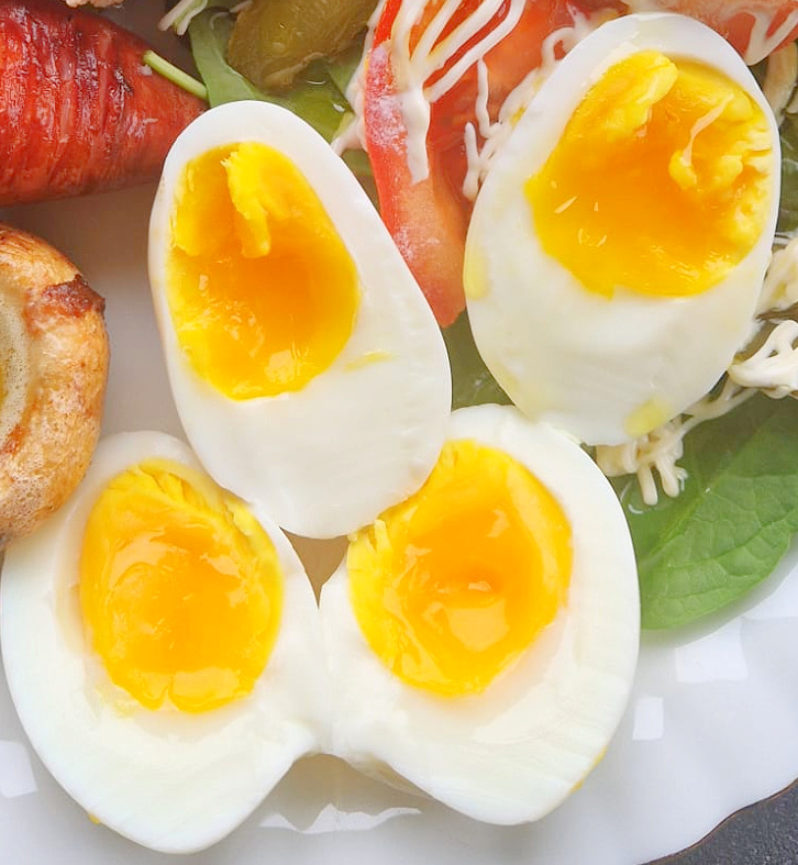 Dwa jajka ugotowane w air fryerze ułożone na talerzu z dodatkami.