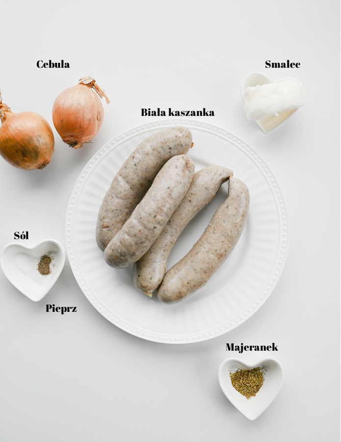 Składniki na farsz do pierogów z białą kaszanką. Białe kaszanki na talerzu, obok cebule, smalec oraz przyprawy na jasnym blacie