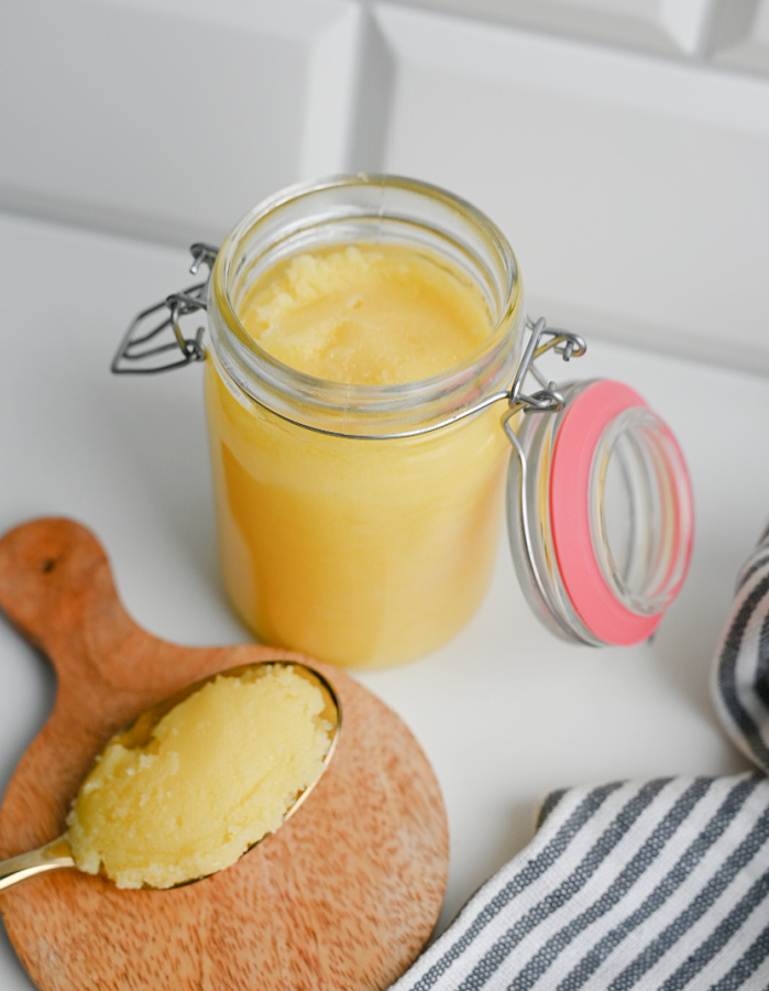 Widok z góry na teksturę zastygniętego masła klarowanego ghee w otwartym słoiku i na łyżce.