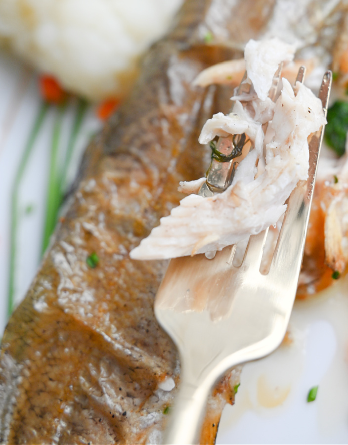 Delikatne, soczyste białe mięso pieczonego pstrąga na złoto-srebrnym widelcu.