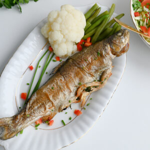 Zdjęcie głowne. Pstrąg z frytkownicy beztłuszczowej serwowany na białym półmisku ze zdrowymi dodatkami.