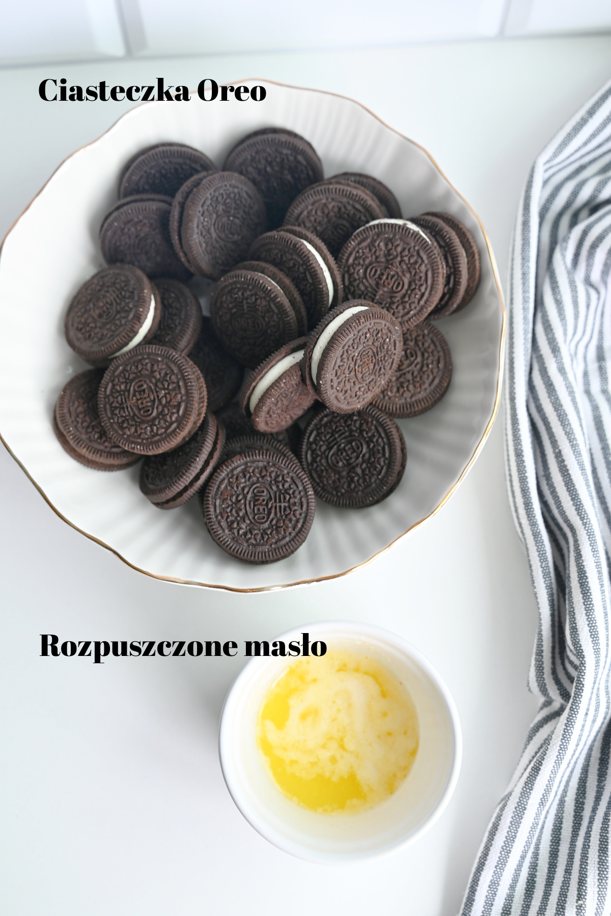 Składniki na spód deseru: miska z ciasteczkami Oreo i miseczka z płynnym masłem na białym tle.