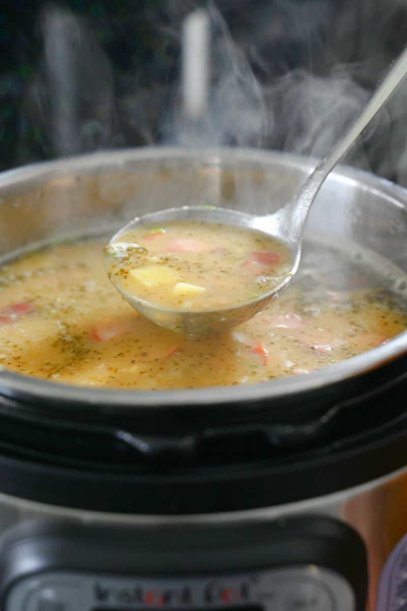 Srebrna chochla nabierająca gęstą zupę grochową z parującego garnka Instant Pot; widoczne kawałki ziemniaków i wędliny.