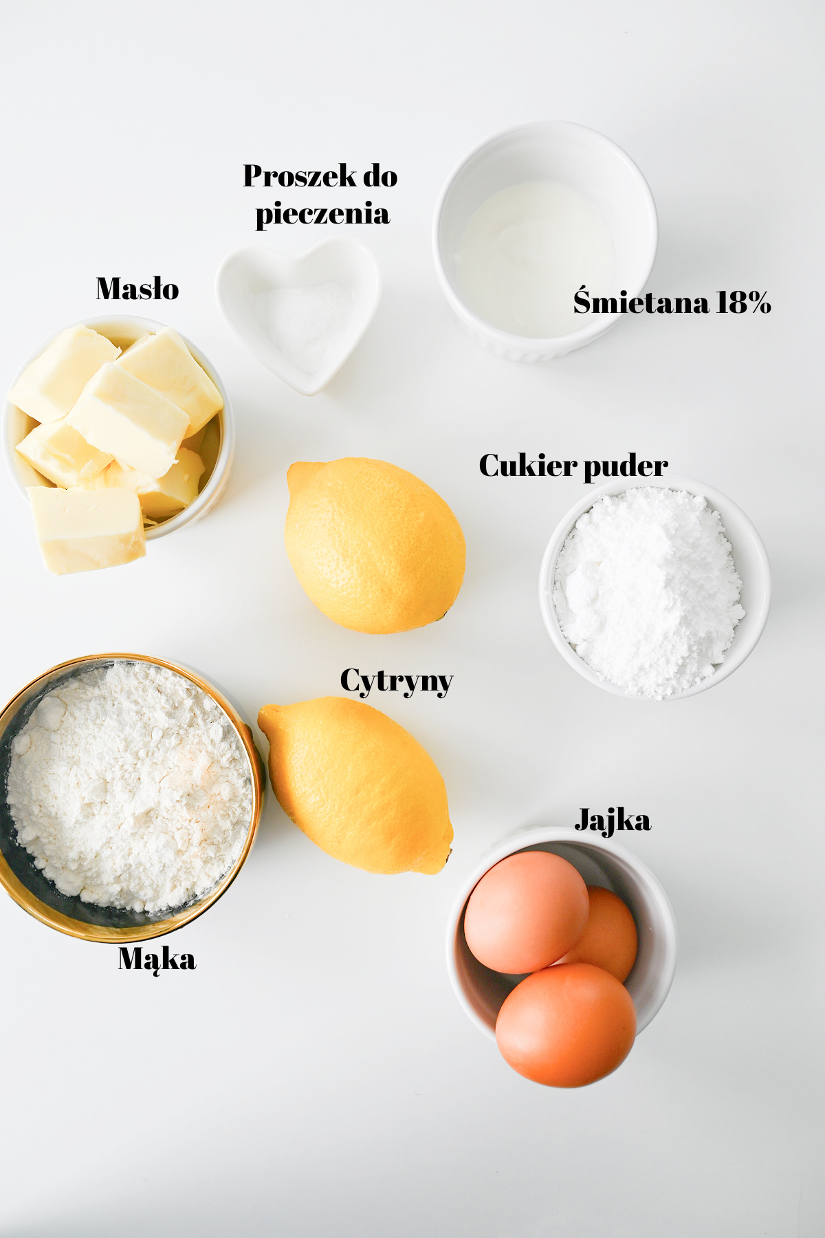 Składniki na ciasto cytrynowe ułożone w miseczkach na białym tle.