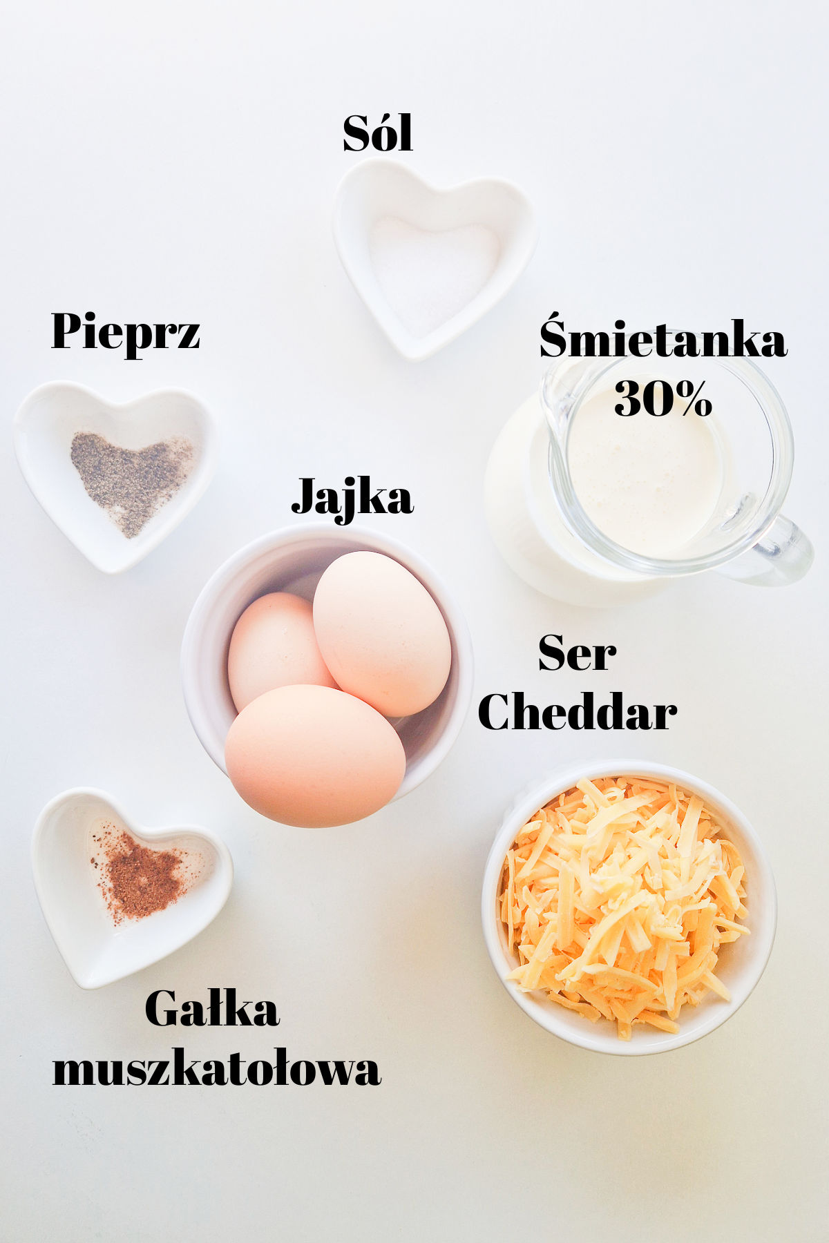 Składniki na masę: jajka w miseczce, dzbanuszek ze śmietanką, miska ze startym serem cheddar i przyprawy.