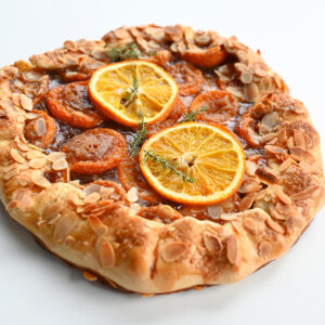 Pieczona rustykalna galette z morelami, plastrami pomarańczy i płatkami migdałów na białym tle.
