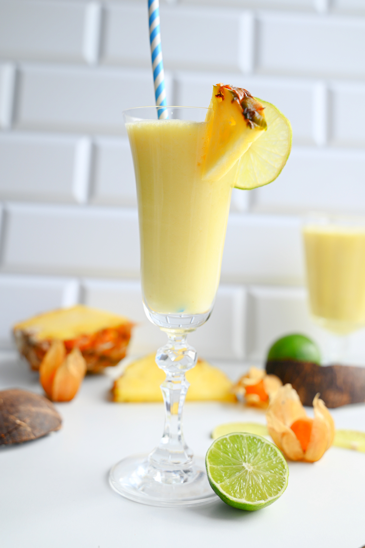 Wysoki kieliszek z żółtym drinkiem Pina Colada, papierową słomką i dekoracją z limonki.