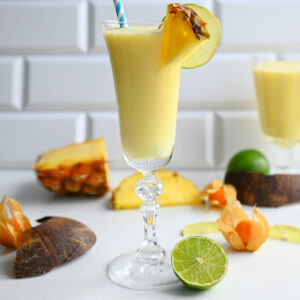 Bezalkoholowa Pina Colada w smukłym kieliszku ozdobionym plastrem ananasa na tle białych kafelków.