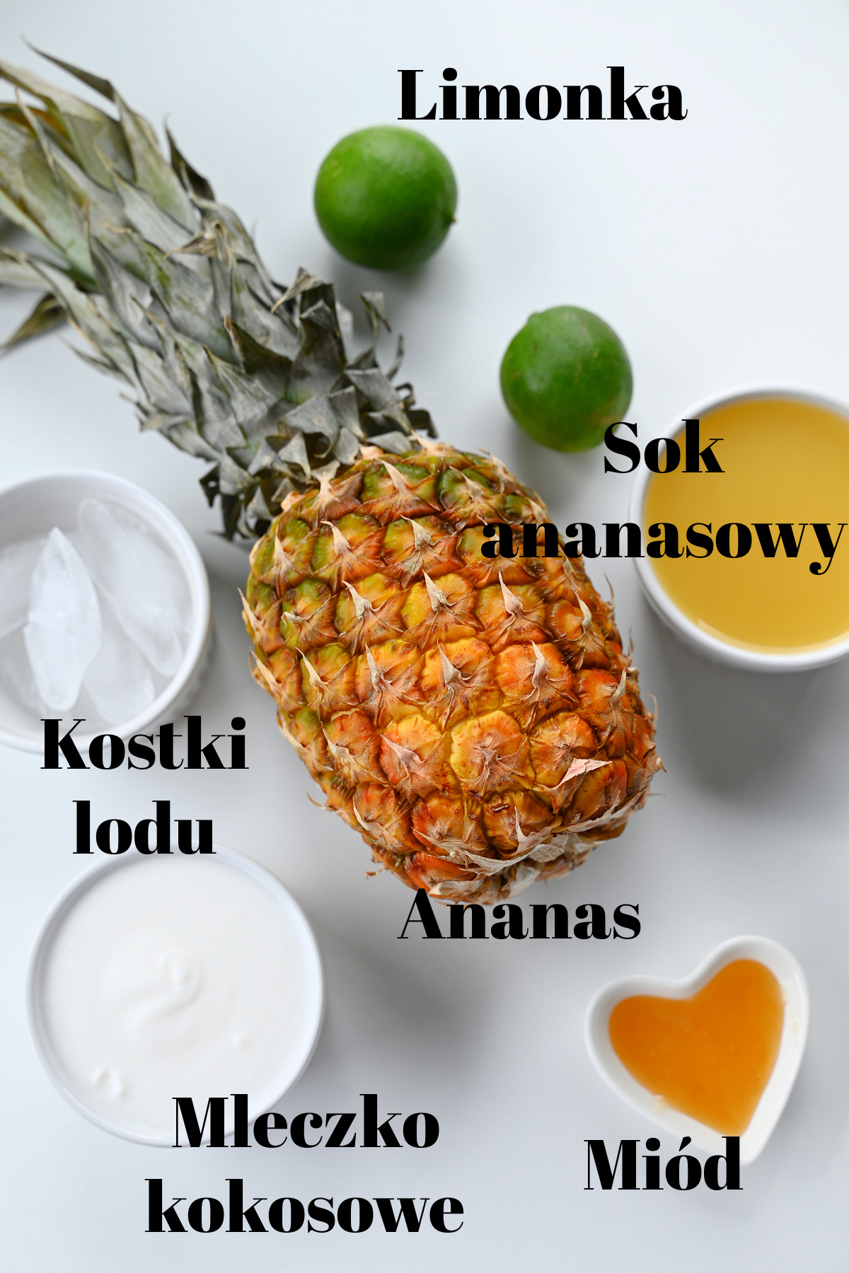 Cały ananas, limonki, sok ananasowy, mleczko kokosowe, miód i lód ułożone na białym tle.