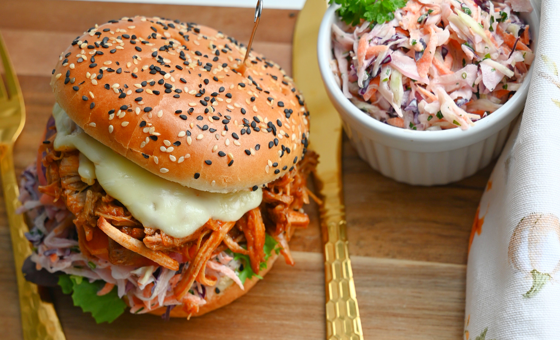 Burger z szarpaną wieprzowiną i colesławem obok miseczki z surówką.