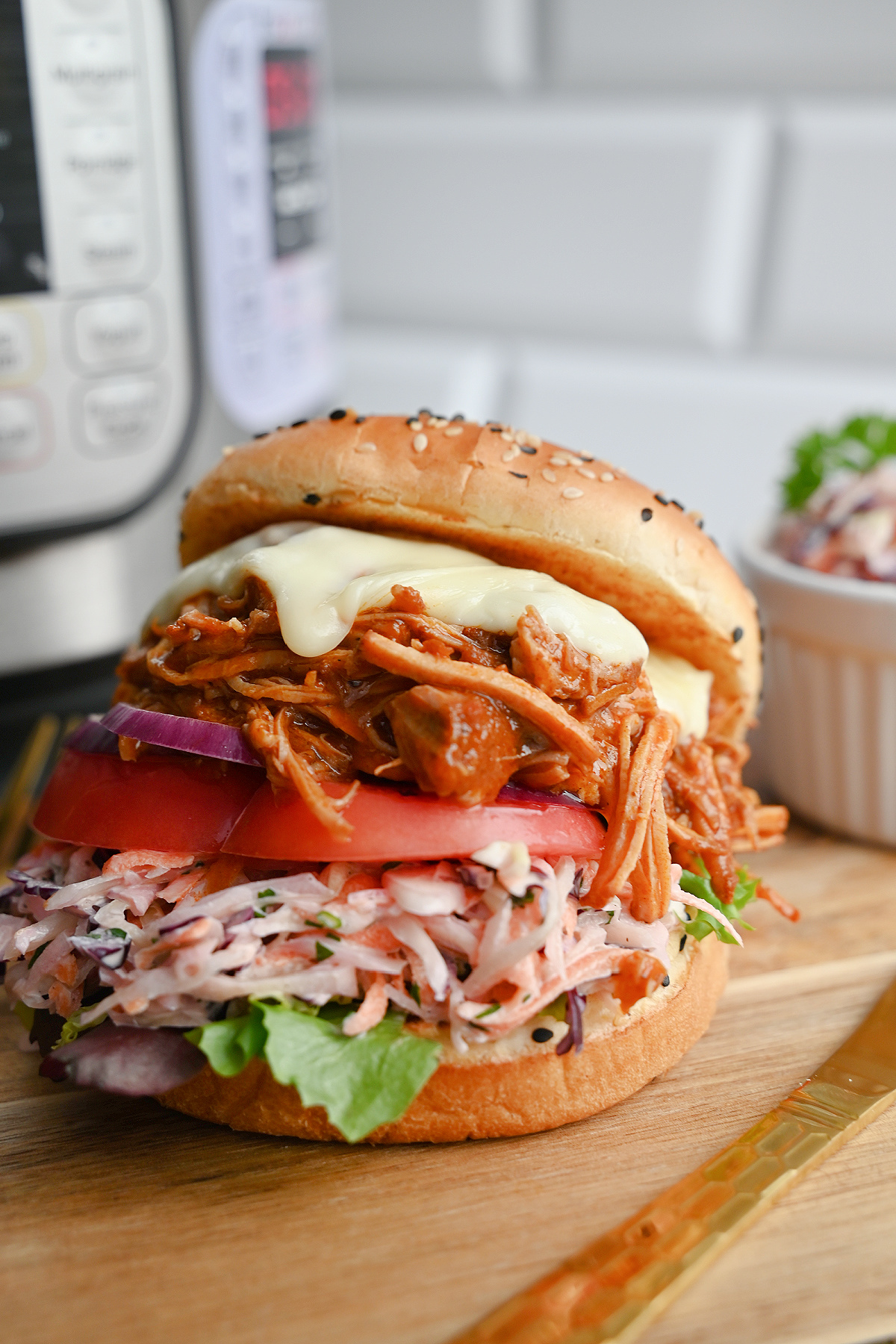 Wysoki burger z szarpaną wieprzowiną, serem, pomidorem i colesławem na drewnianej desce.