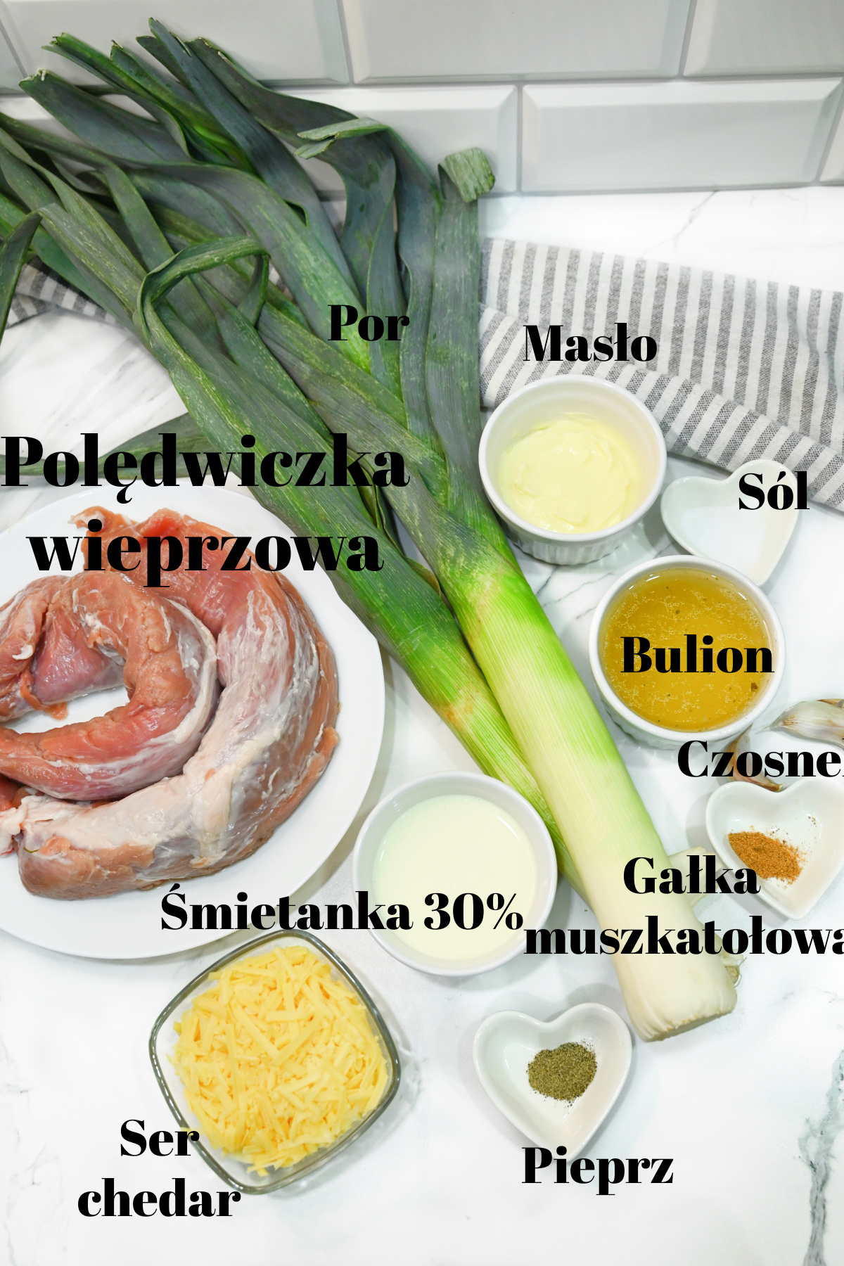 Składniki do polędwiczki w sosie serowo-porowym ułożone na jasnym blacie z czarnymi podpisami.